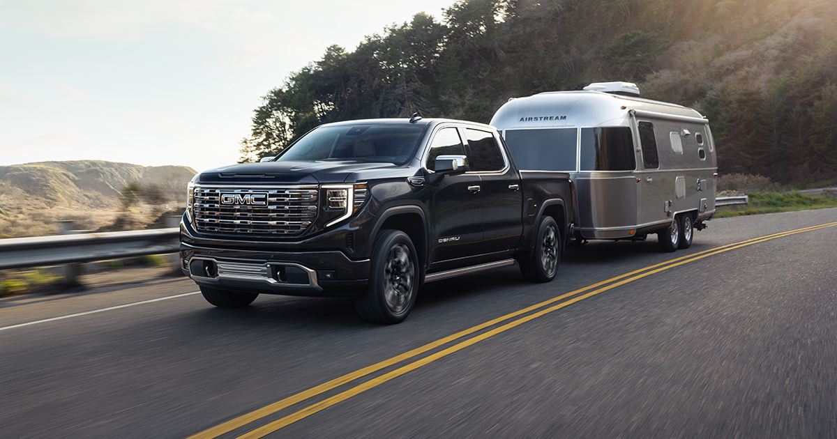 A black GMC Sierra 1500 towing a trailer driving on the highway.