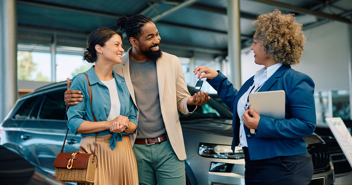 A salesperson at the dealership handing keys to a smiling couple